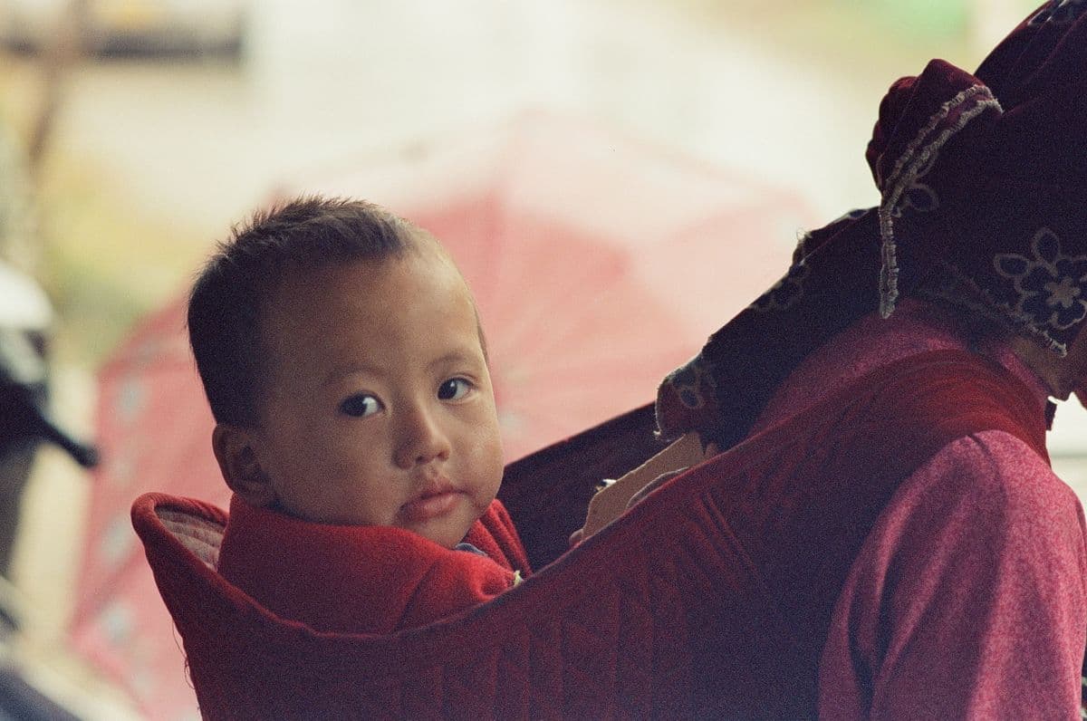 A caregiver carrying a child in a back carrier