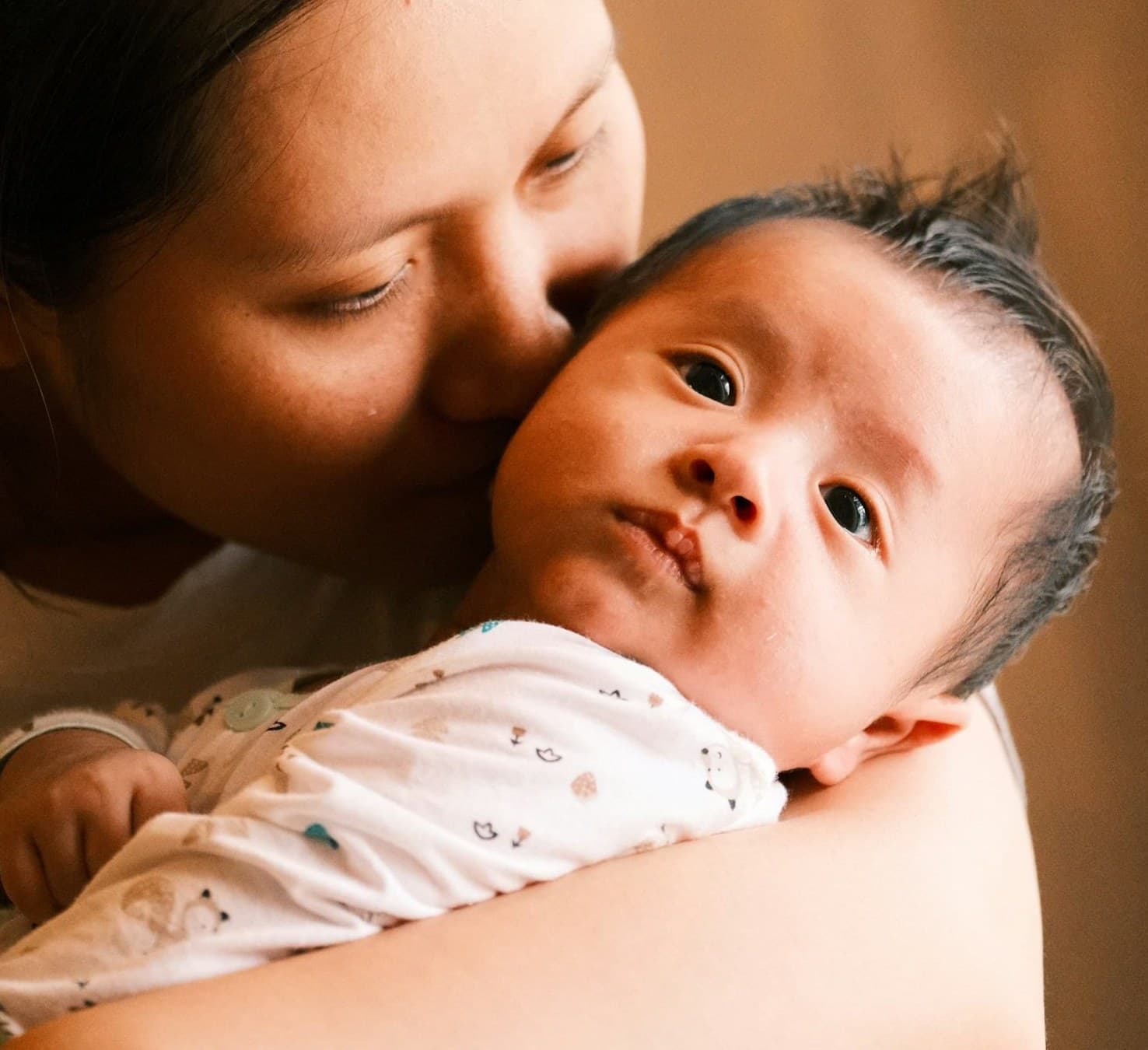 A parent holding a young baby cheek to cheek, the baby looking out toward the camera